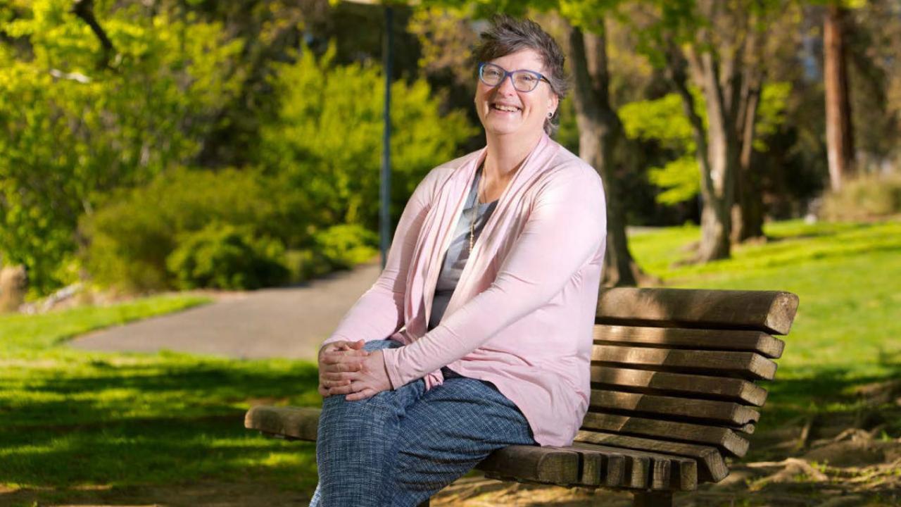 Dean Lauren Lindstrom, casually sitting on bench in the arboretum.