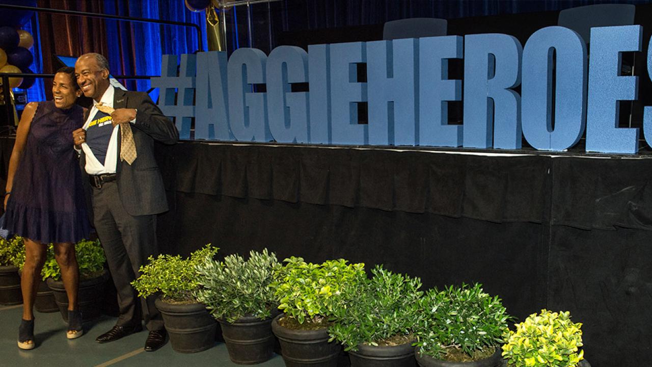 LeShelle and Gary May pose with a large sign that reads #AggieHeroes