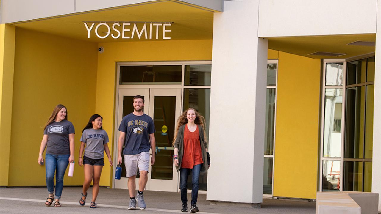 Four students in front of main entrance of new residence hall