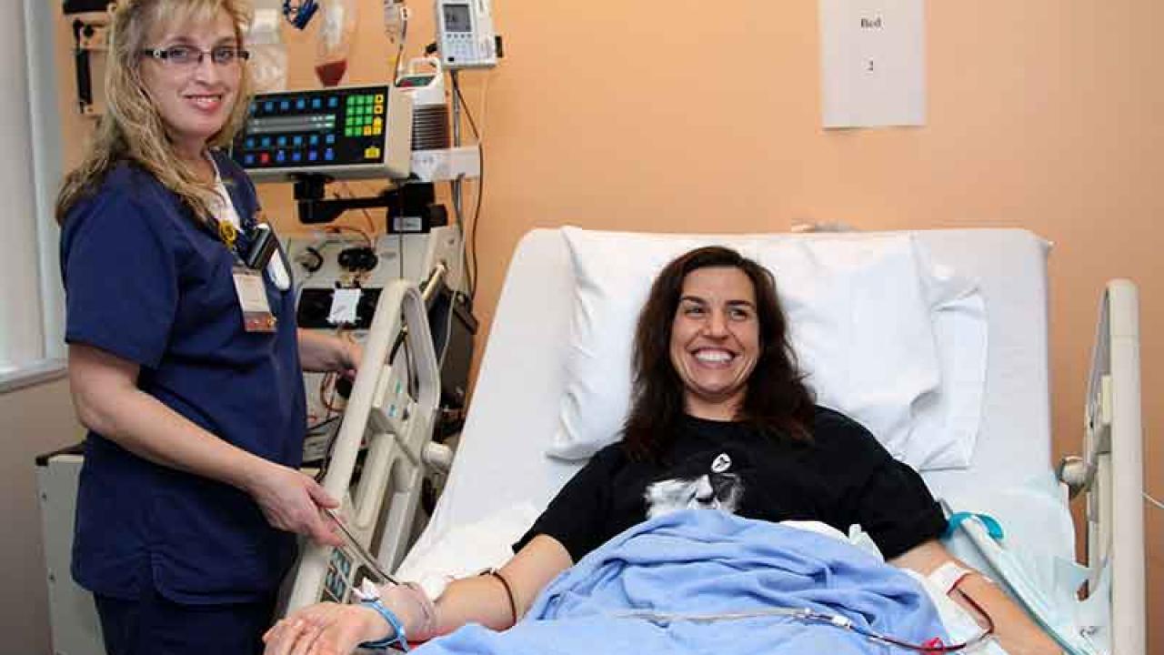 Photo: Apheresis nurse Natalie Detwiler stands beside hospital bed; Joanna Friesner is in the bed, with tubes in her arms for stem cell donation.