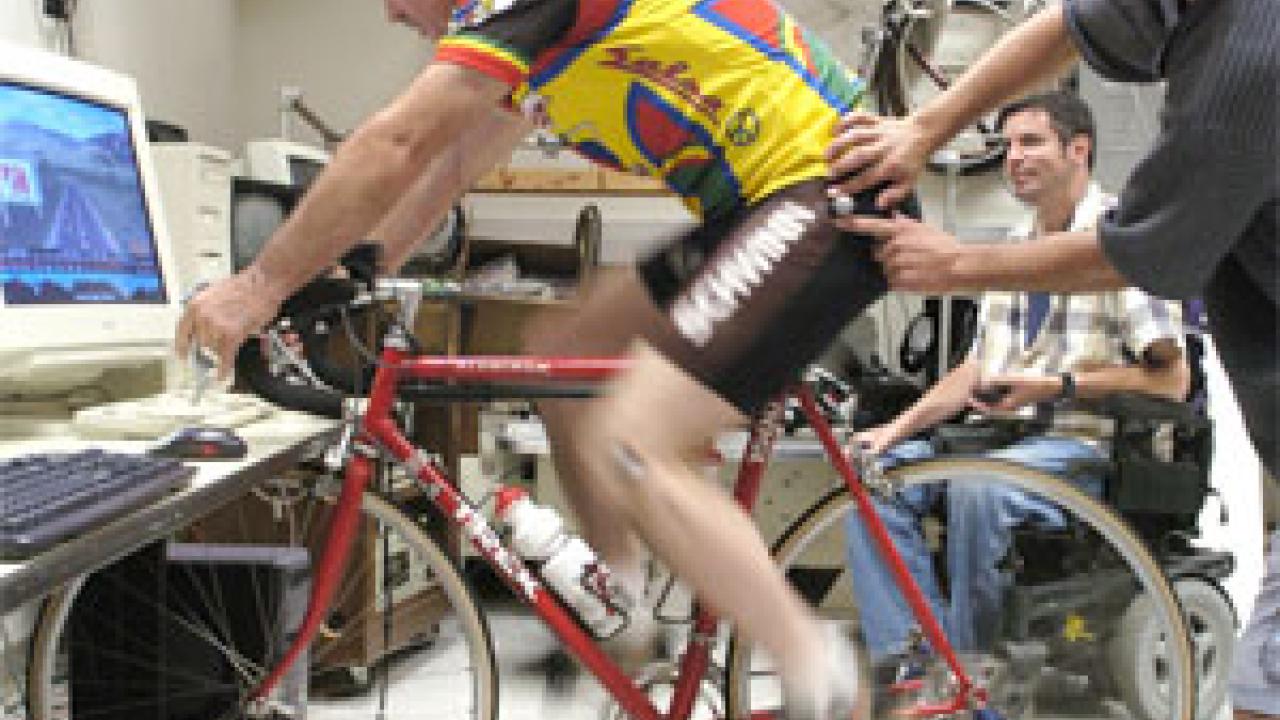 Maury Hull spins the pedals on his Computrainer while doctoral candidate Matt Camilleri affixes a third reflective globe that will help wall-mounted sensors create a 3-dimensional map of the rider&rsquo;s movements while cycling. The Computrainer si