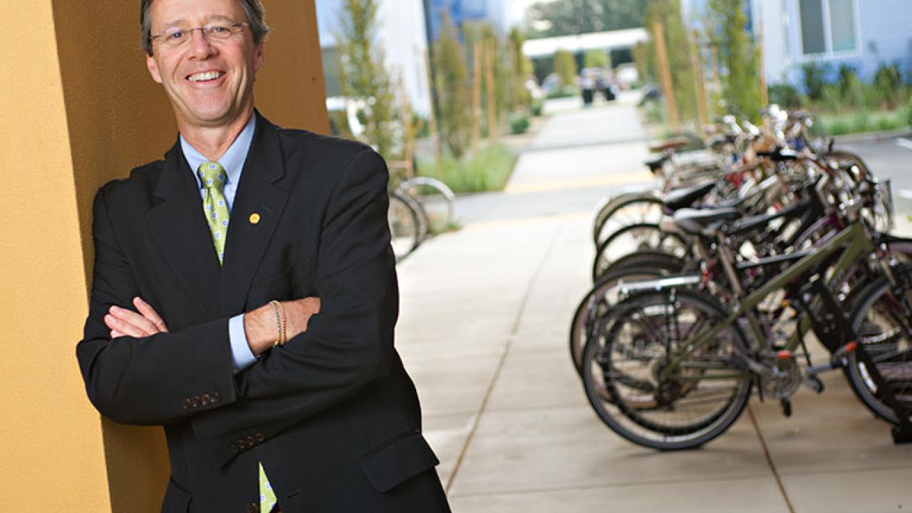 Photo: Vice Chancellor John Meyer, leaning against a building, with bicycle rack in background
