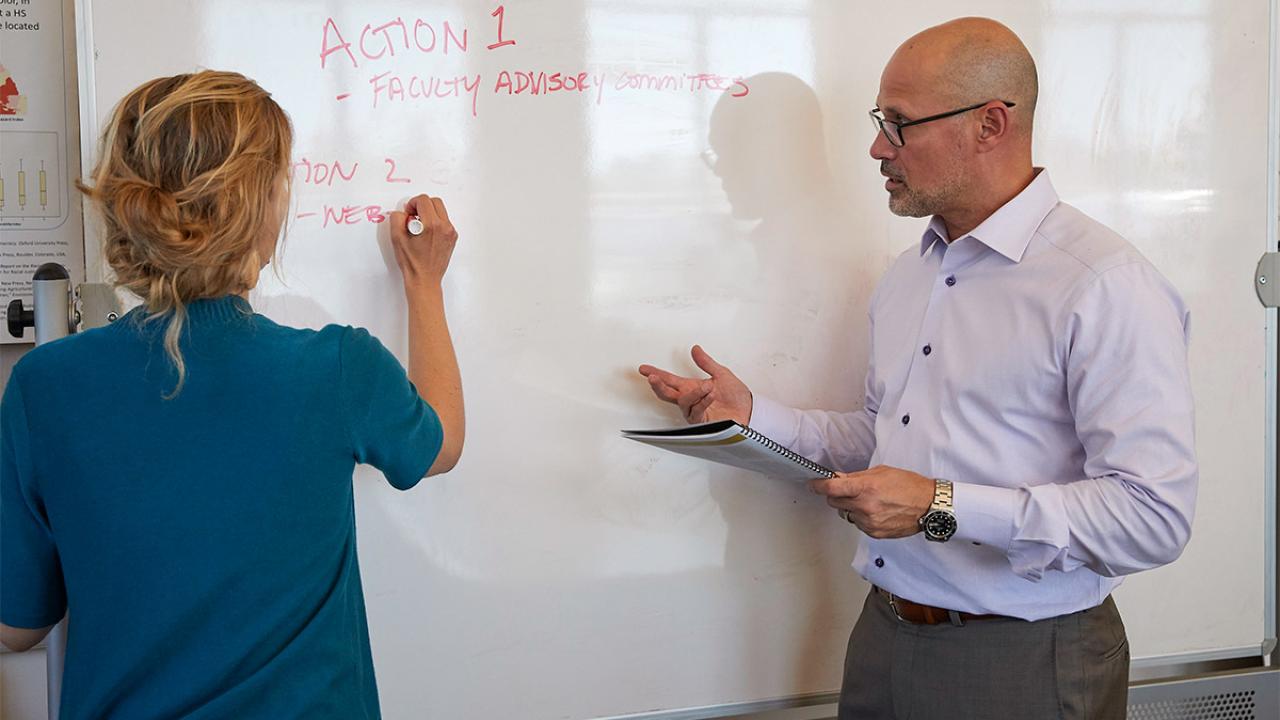 Michael Rios speaking to woman who is writing on a whiteboard.