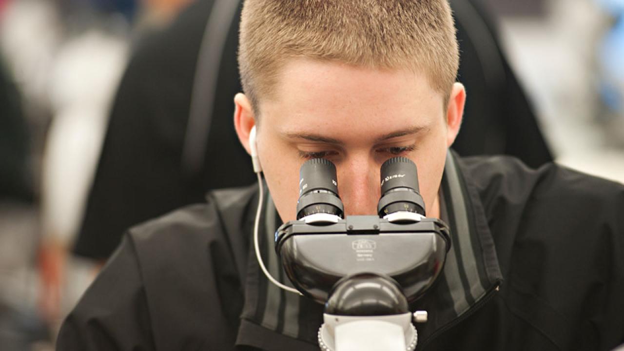 A male student looks into a piece of scientific equipment