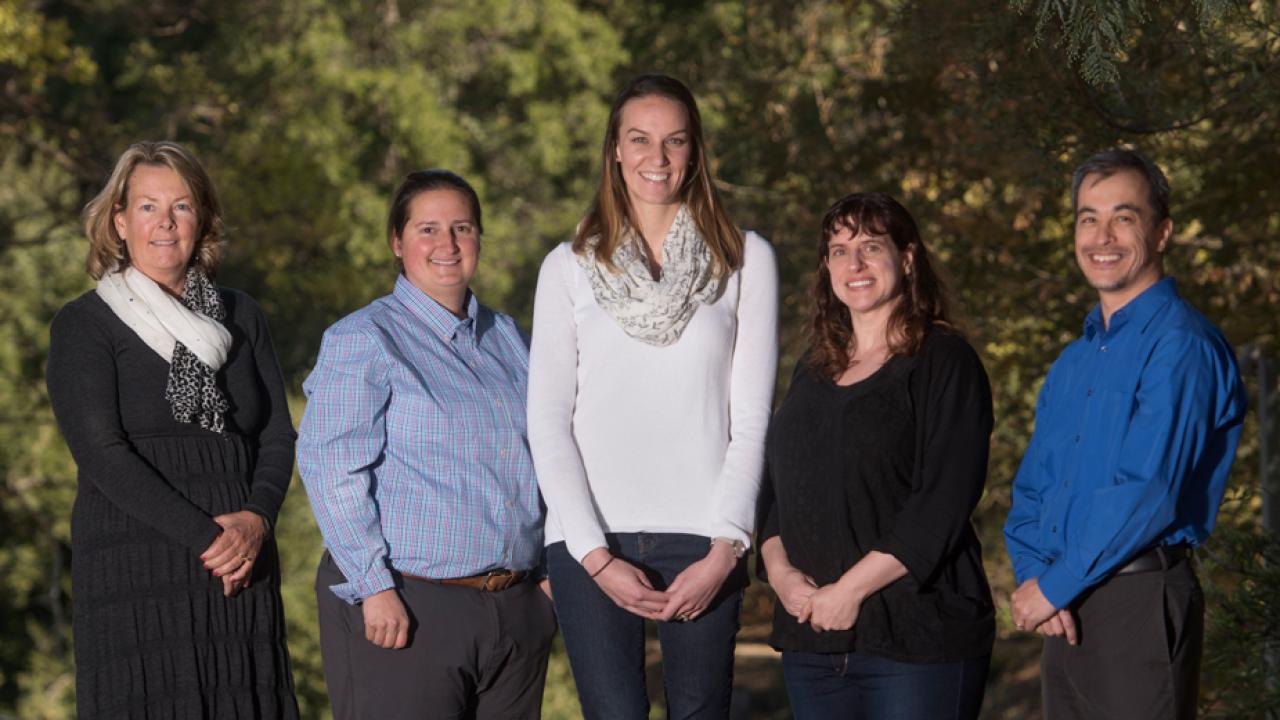 Portrait of five academic advisors, posed in a line, in the arboretum