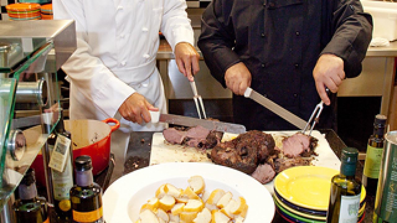Two men cooking, with bread and olive oil in the foreground