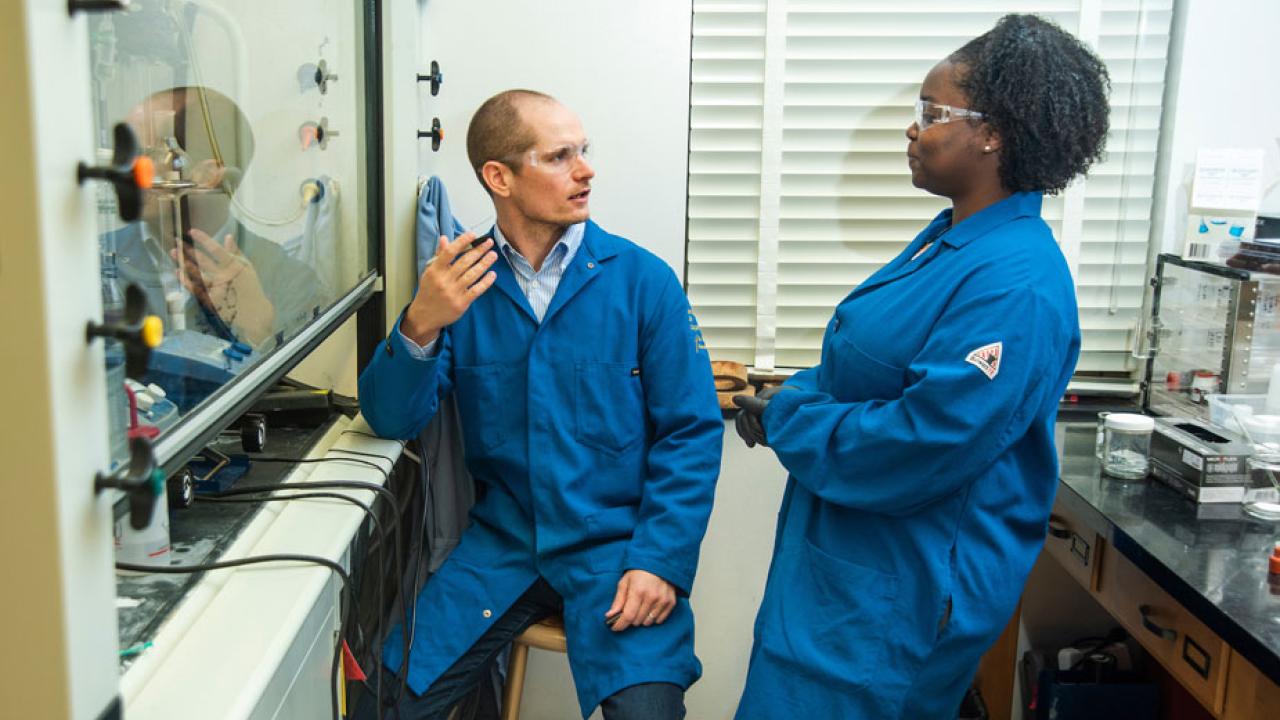 Man and woman in blue lab coats, in a chemistry lab.