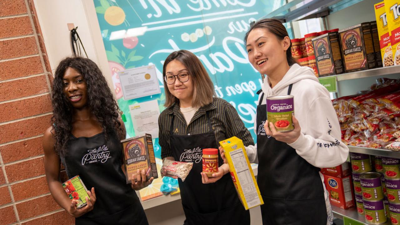 Three student interns, holding food items at the Pantry.