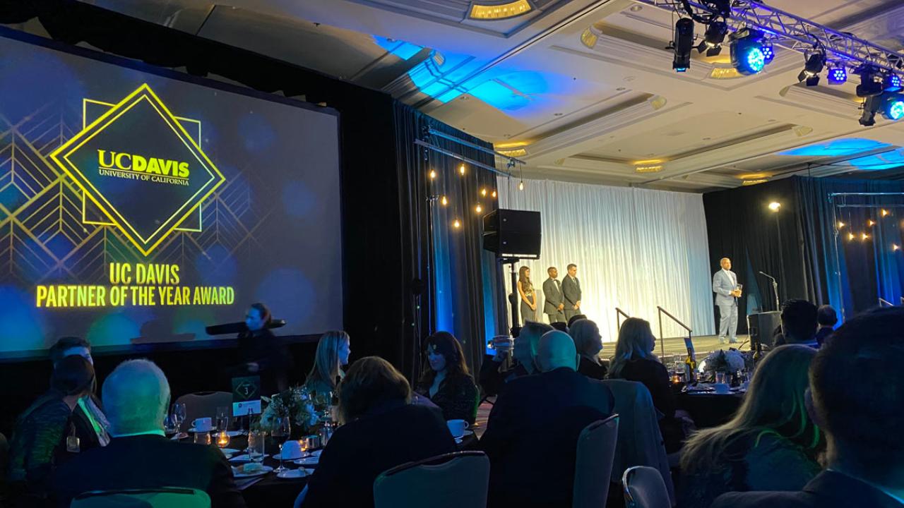 View from audience, showing "UC Davis Partner of the Year Award" projected on screen and Chancellor May at microphone..