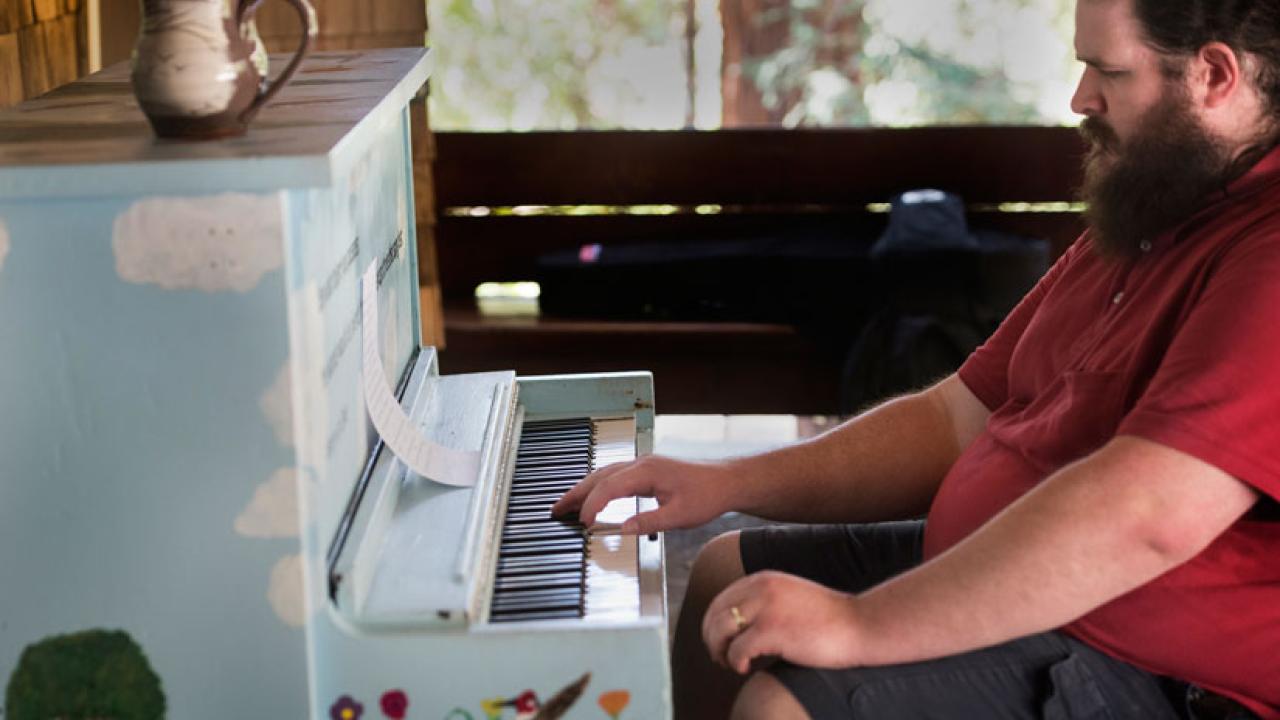Photo: Man playing piano on Wyatt Deck, amid Folk Music Jam Session.