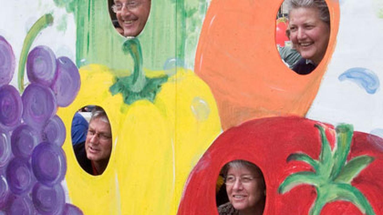 Photo: Four people looking out of a board painted with vegetables