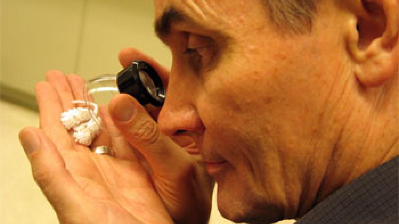 photo: man examining white objects in hand with a loop