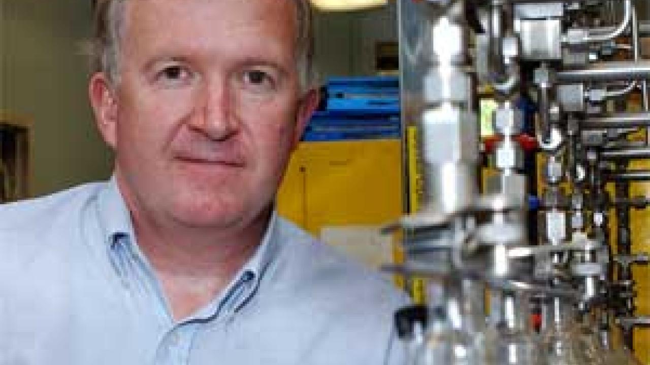 Photo: portrait of man standing next to glass bulbs in lab