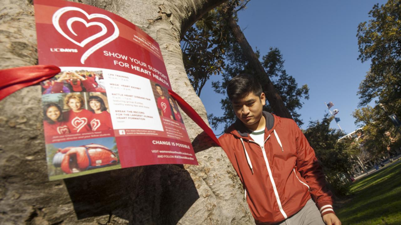 Photo: Student next to tree with red ribbon and a poster