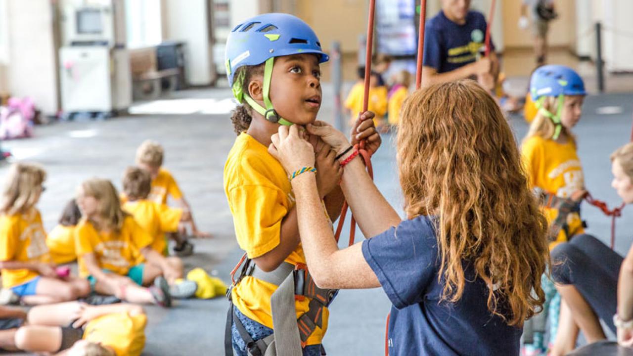 Wall-climbing class: Adult buckles girl's helmet.