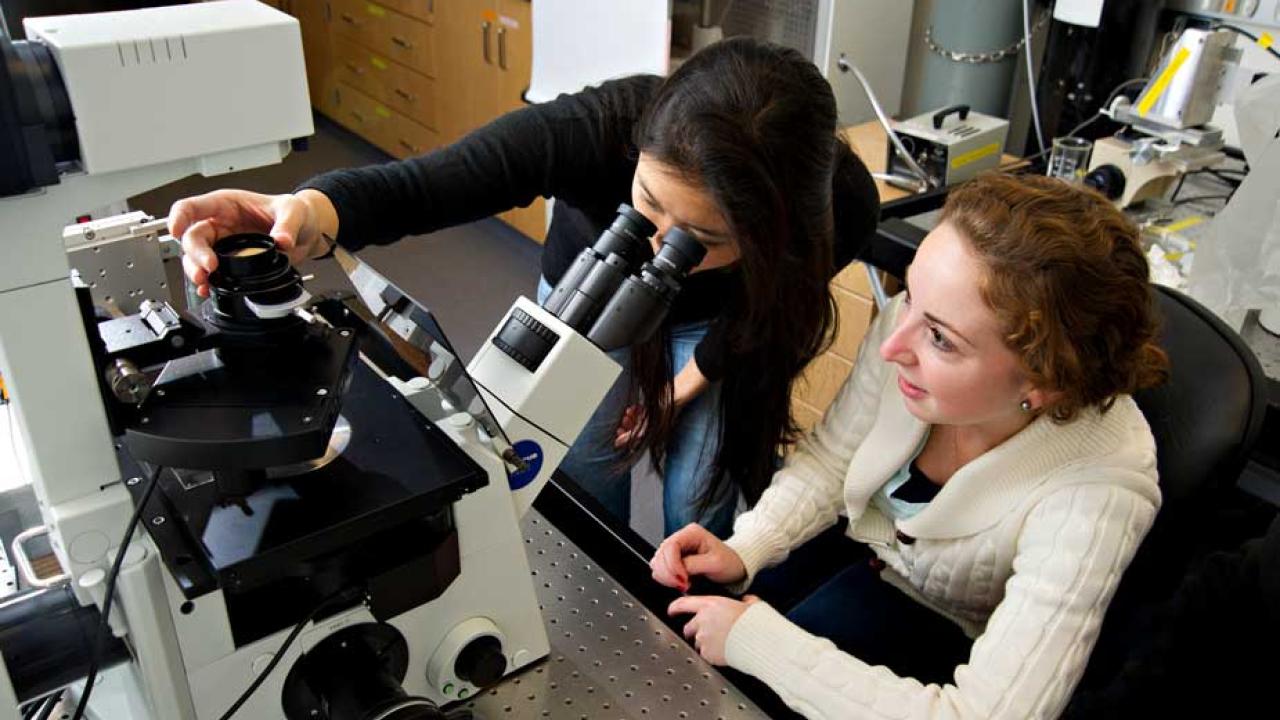 Two women at microscope table in lab.