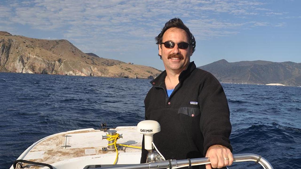 Man on boat in water with bare hills behind