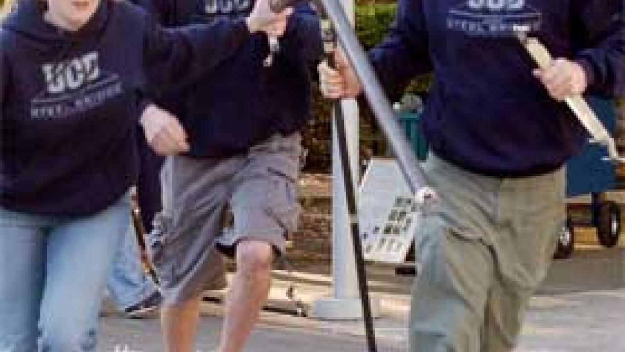 Photo: Woman and two men in hard hats carry bridge parts on the run