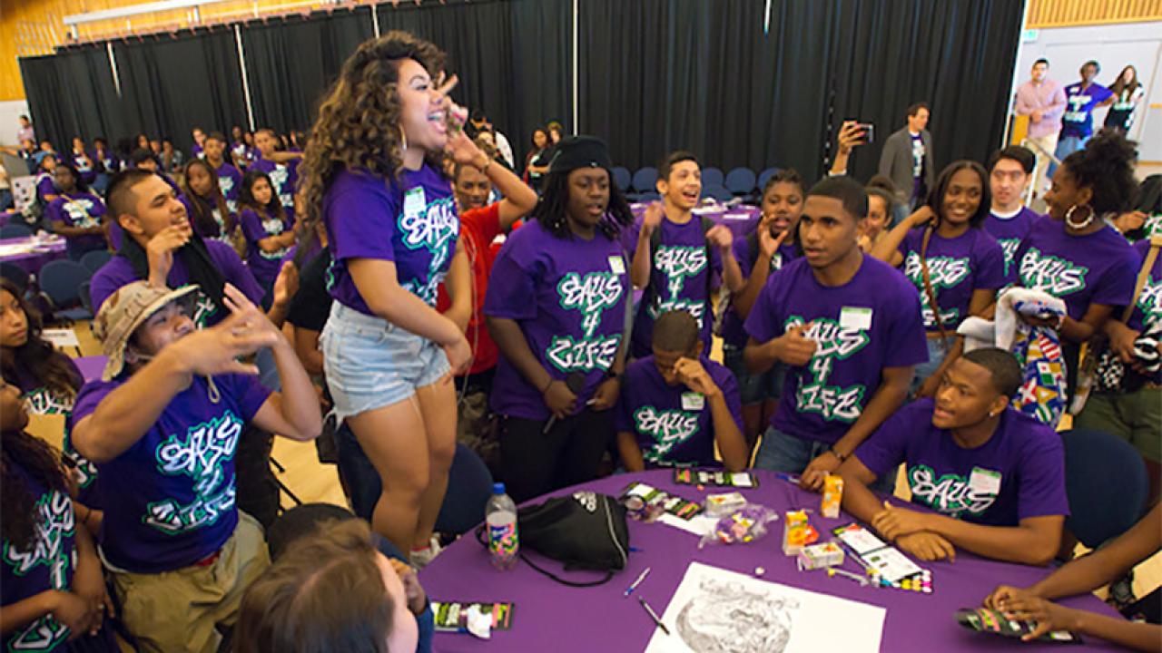standing female student performs among large group around her
