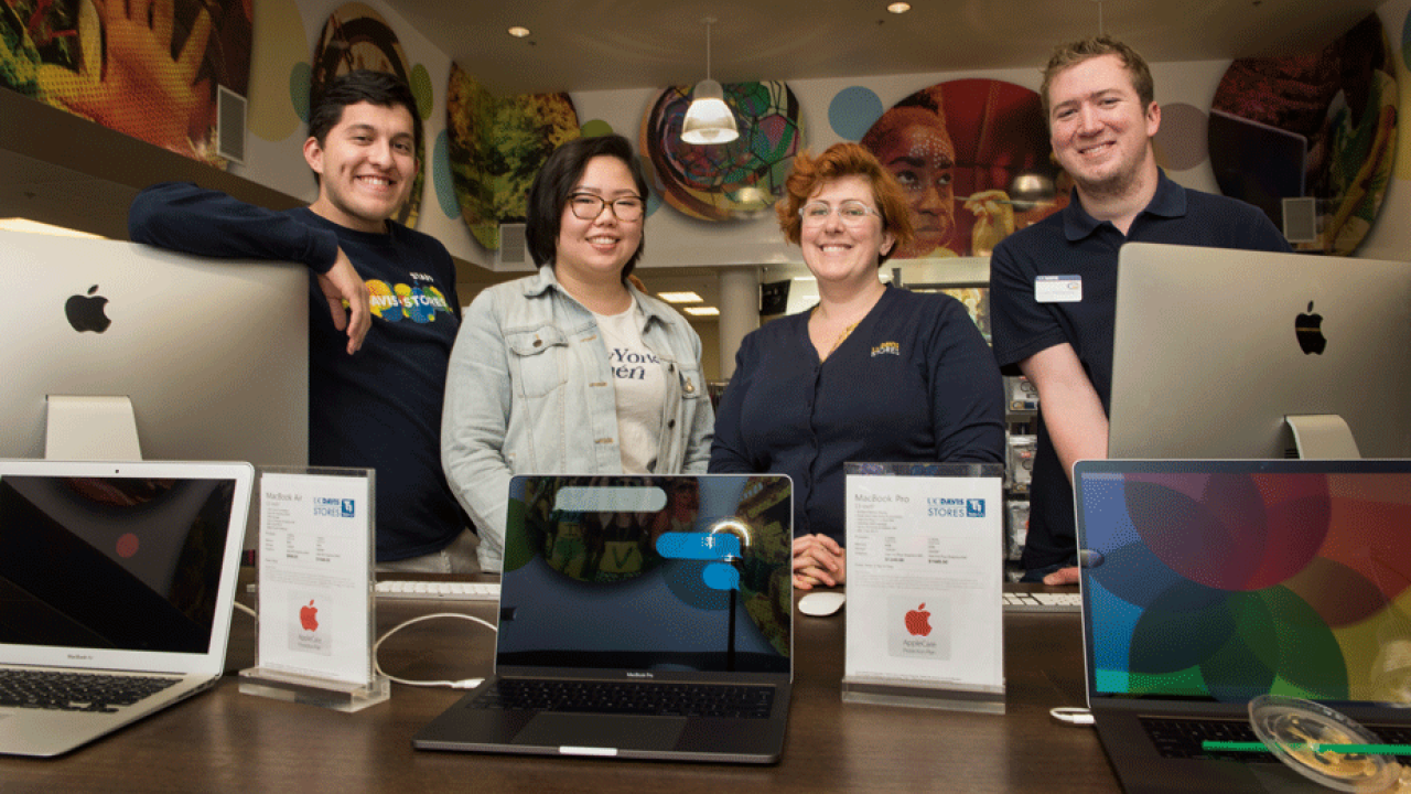 Four employees pose behind computer display.