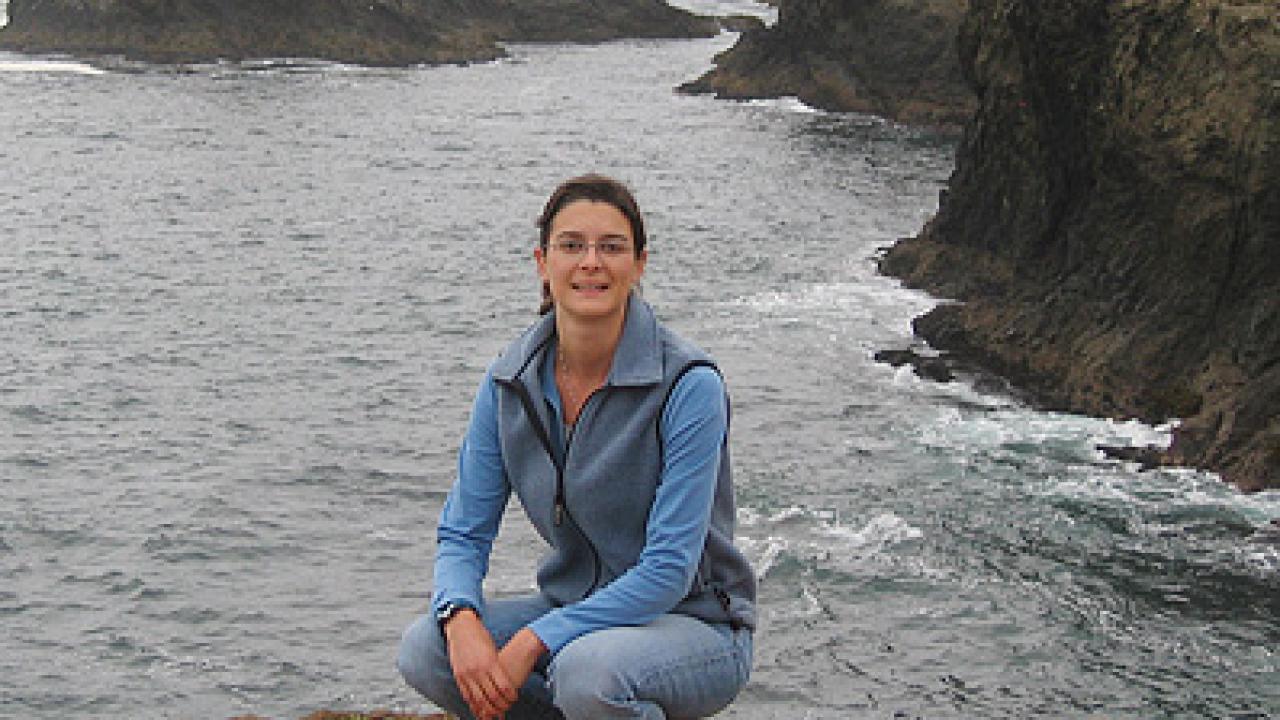 Woman squatting on a cliff's edge at the ocean