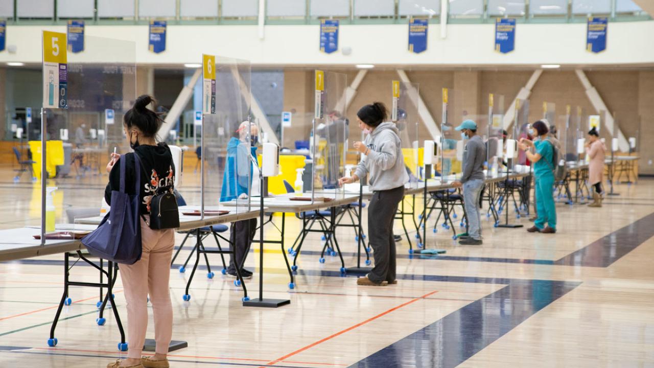 Long counter in gym with plastic dividers separating employees from people submitting saloiva samples.