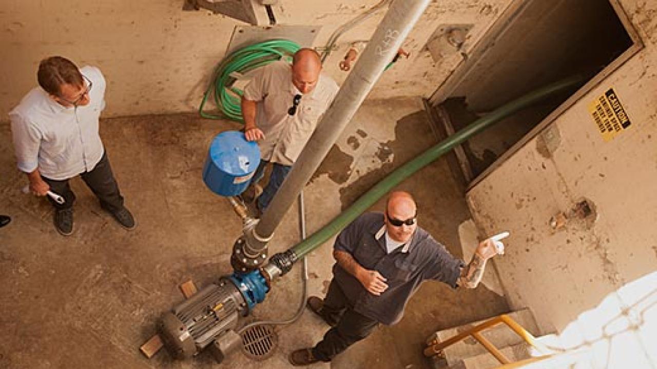 Photo shot from above showing three men in a room with a hose connection