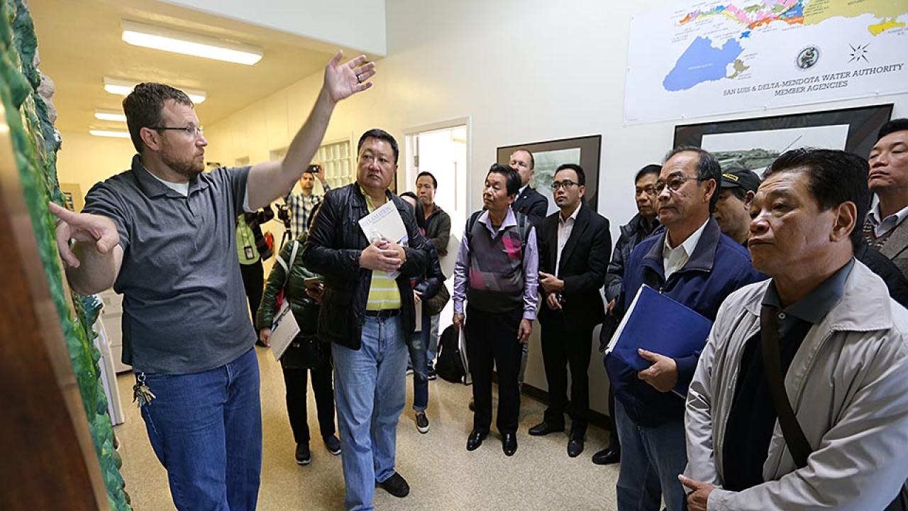 Man points to large wall map as he speaks to group of people in hallway