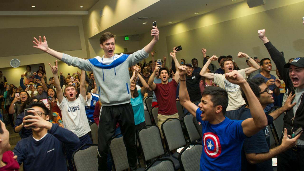 Student stands on chair in celebration.