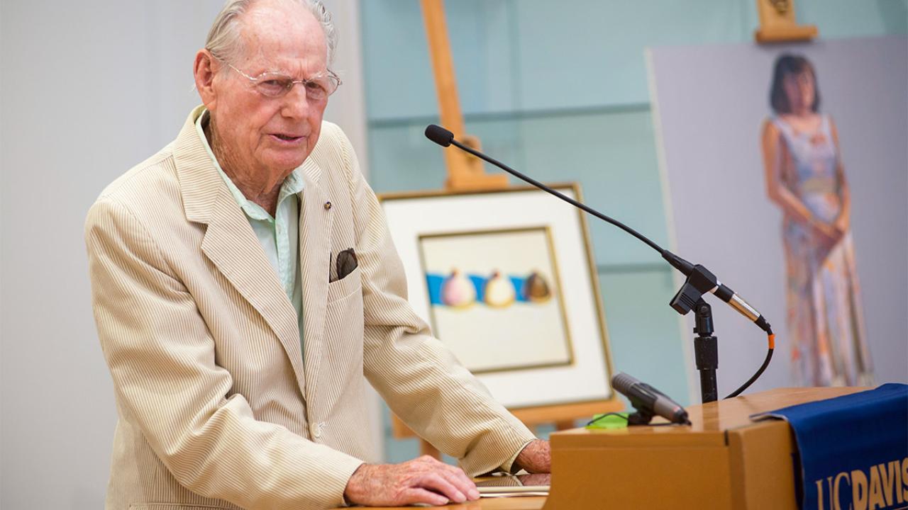 Wayne Thiebaud speaks in front of two of his paintings.