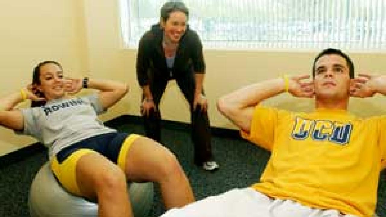 Photo: Woman guiding man doing exercise with another woman with feet in foreground