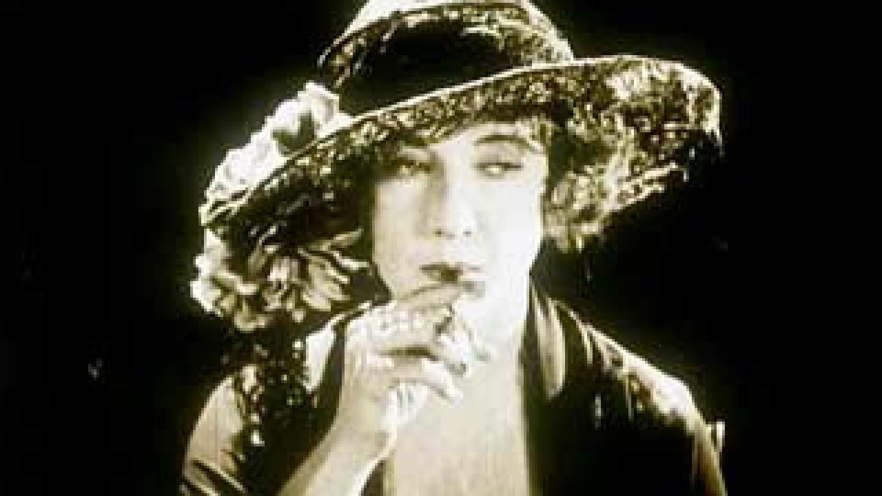 Screenshot from a 1924 film of a woman in a feathered hat smoking a cigarette