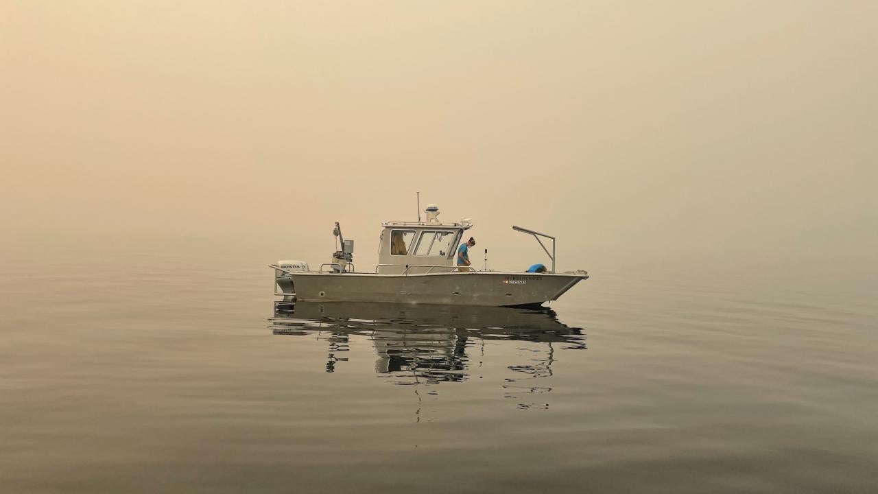 Researcher Brandon Berry from the UC Davis Tahoe Environmental Research Center collects data from a research vessel on the water at Lake Tahoe amid smoke-filled skies. 