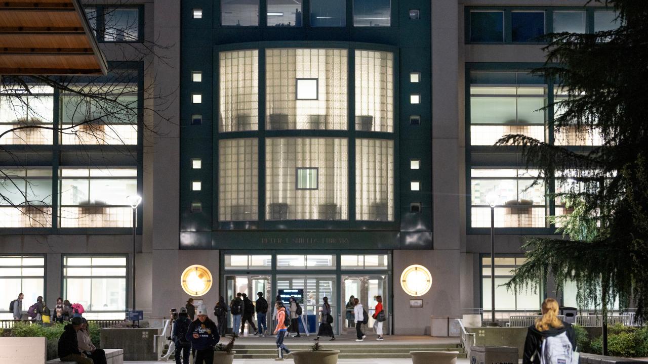 students moving in and out of library on UC Davis campus at night with light pouring through windows.