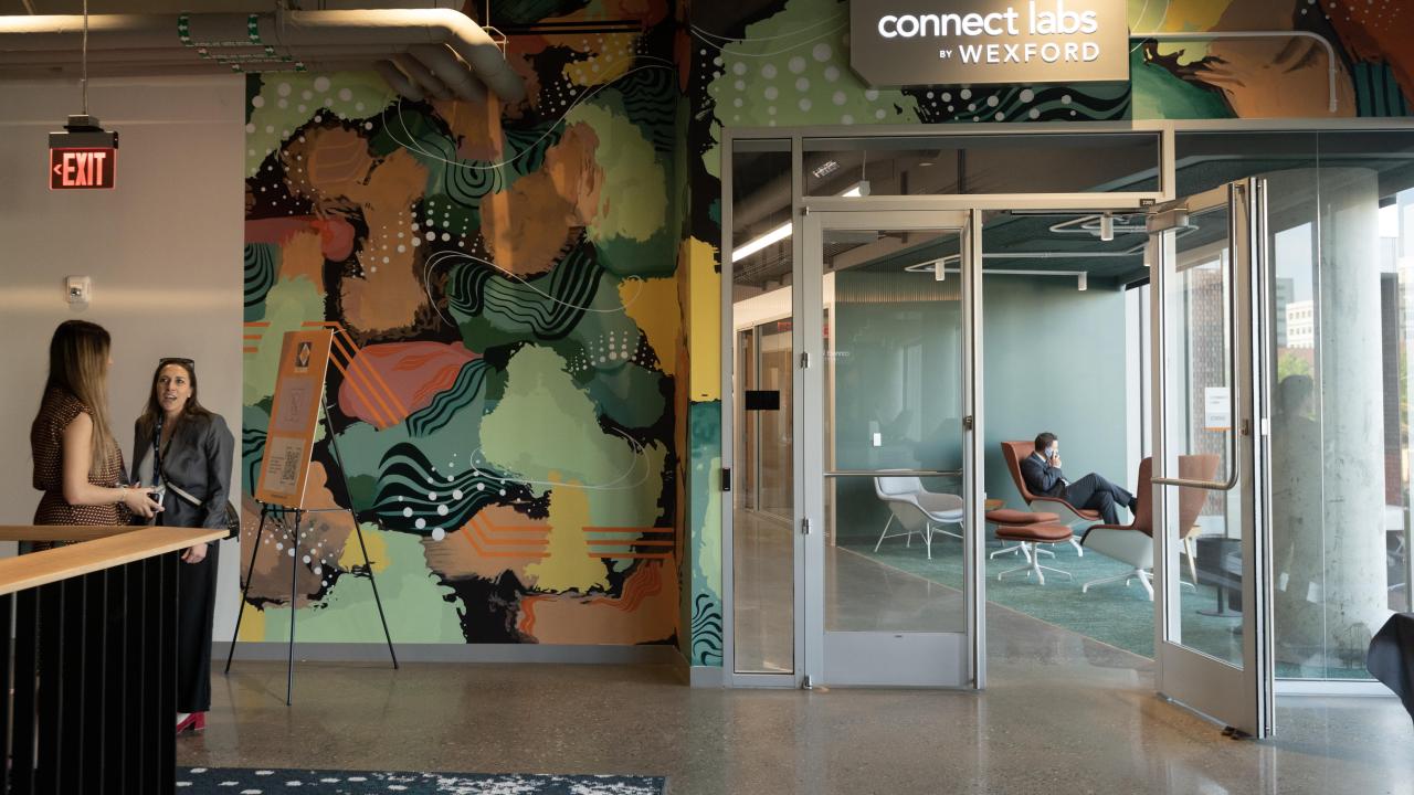 People talk outside of a brightly decorated office labeled "connect labs by WEXFORD" 