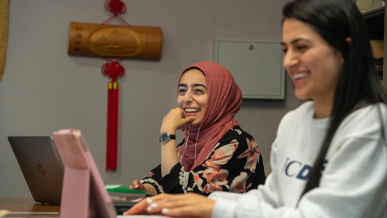 Two students smile at their laptops at UC Davis. 