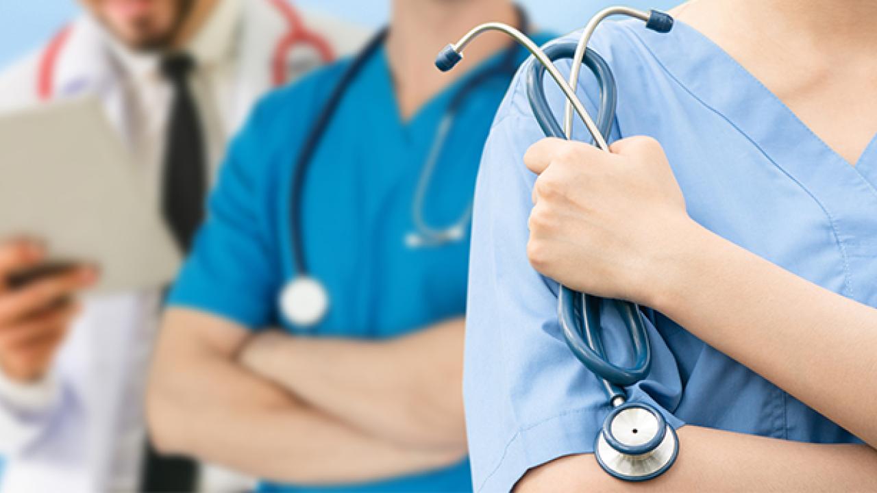 Health professions students from disadvantaged backgrounds often faced childhood adversity, a UC Davis study suggests. Three health professionals in white lab coats and blue scrubs stand next to each other. One holds a stethoscope.