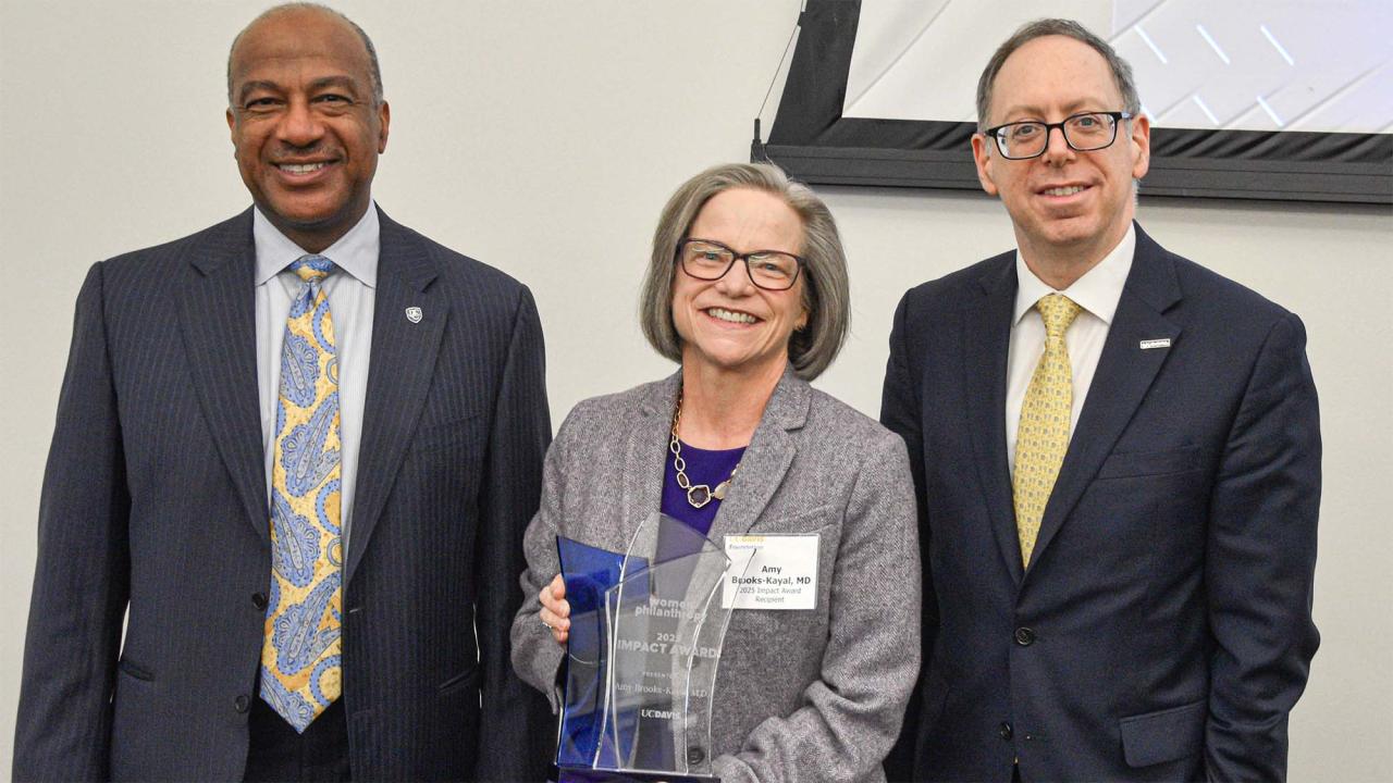 Three people pose for a photo with an award