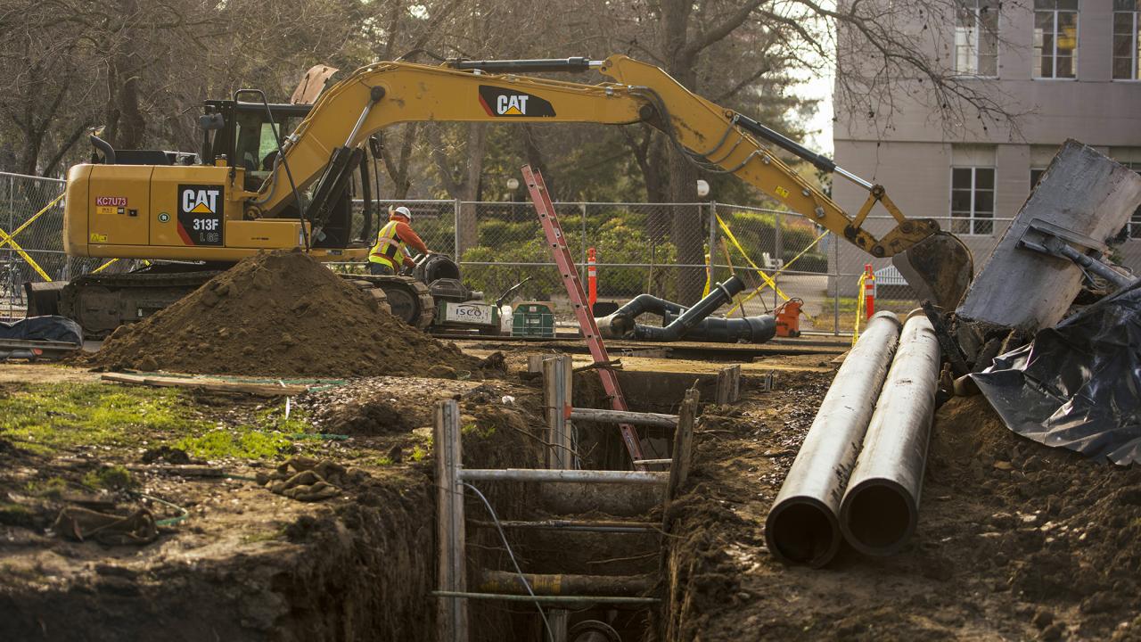 A big trench on the Quad with large underground pipes and a yellow excavator in the background