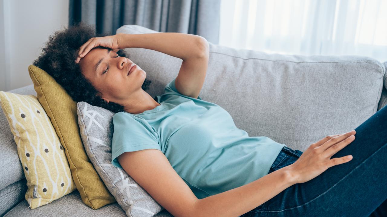 Person reclining on couch holding head as if she has a headache