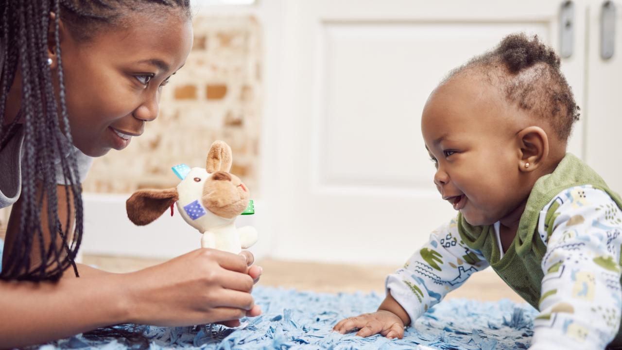 mother holds stuffed animal for baby on blue blanket