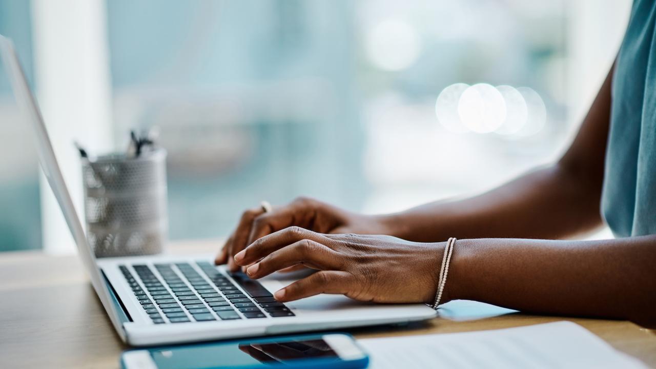 Stock image of a person using a laptop computer. The person's arms and hands are visible. 