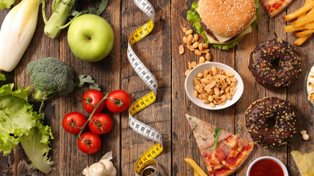 Low-fat veggies and fruits like broccoli, apples, tomatoes shown on left and high-fat foods like hamburgers, pizza and french fries on the right. A tape measure divides the two sides. UC Davis researchers find that switching from a high-fat to a low-fat diet slowed precancerous changes in the pancreas of mice. (Getty)