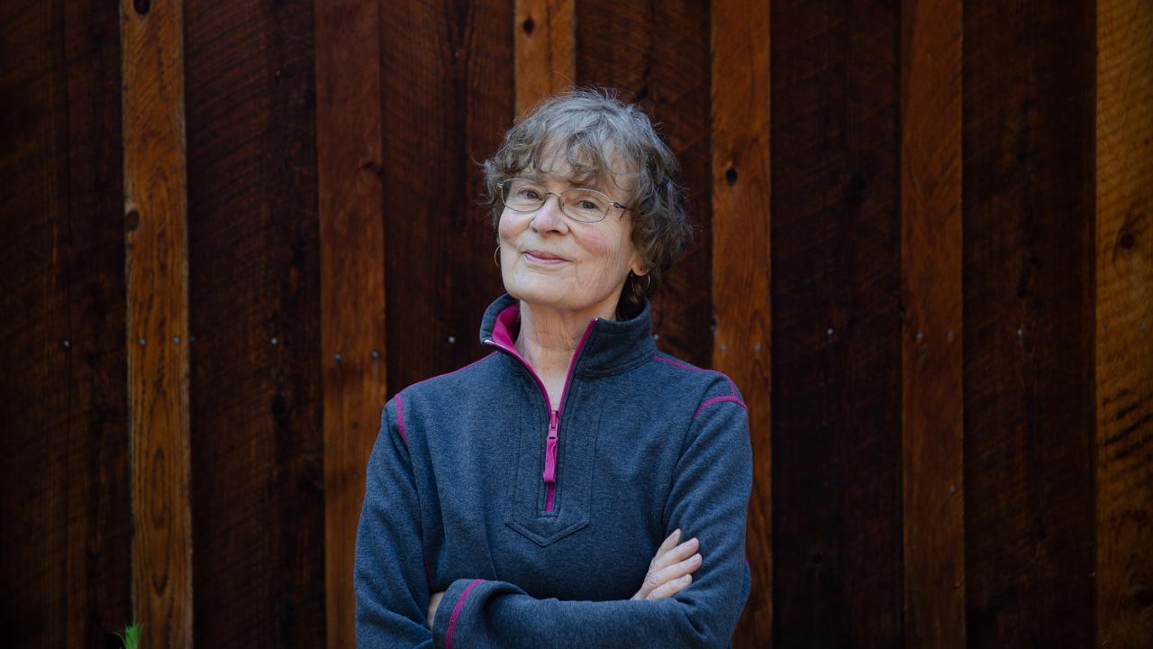 A woman stands in front of a wooden fence.