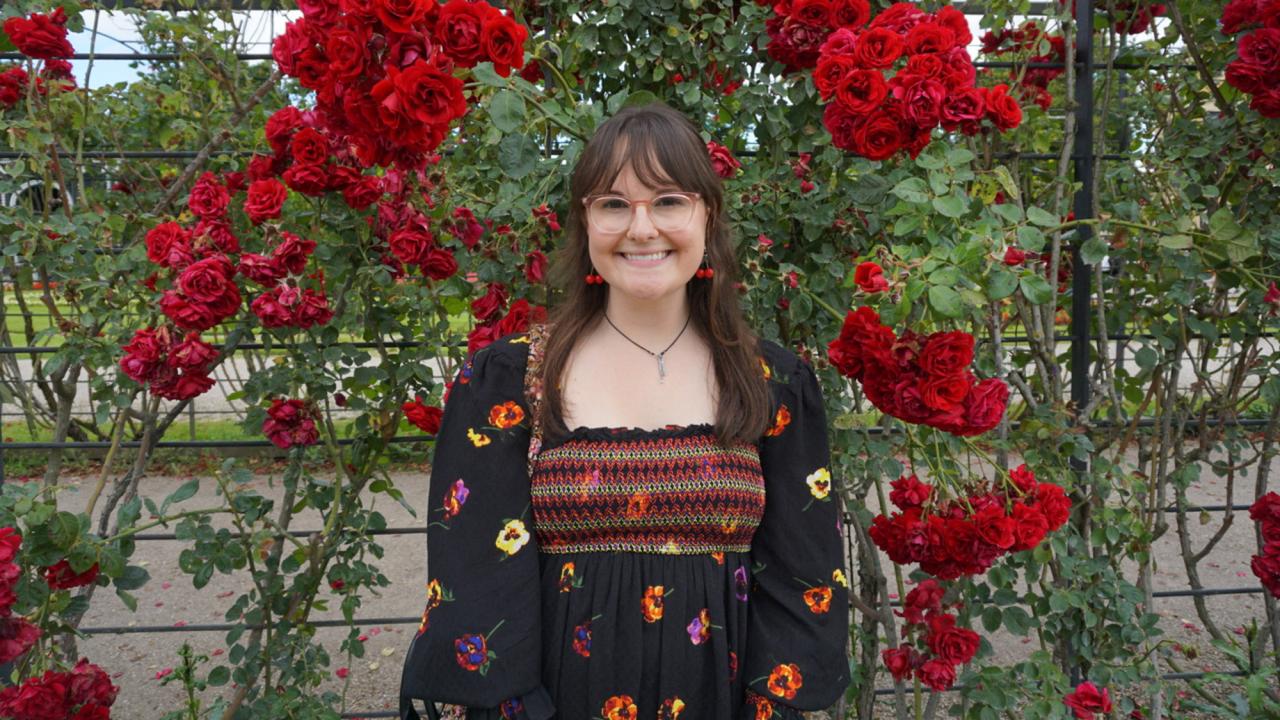Woman stands in front of a wall of flowers