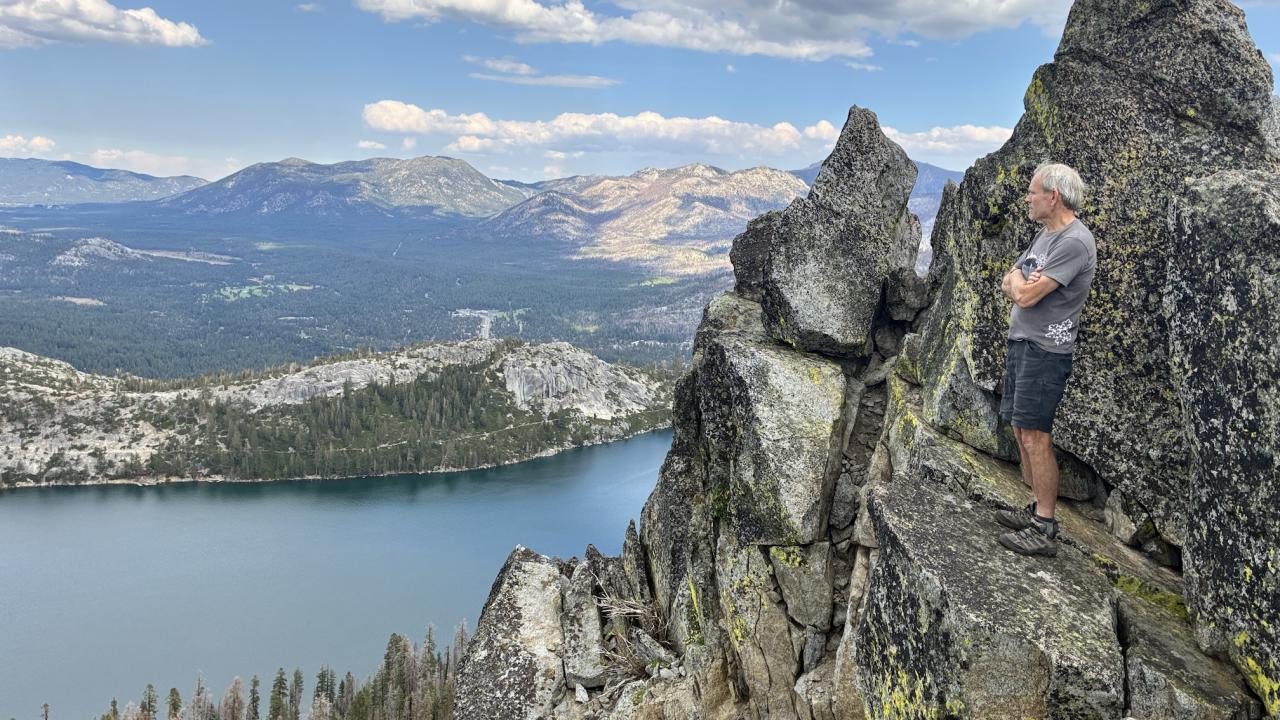 Hugh Safford overlooks Echo Lake. He stands with arms folded along rocky ridges. The lake is below and mountains are int backdrop.