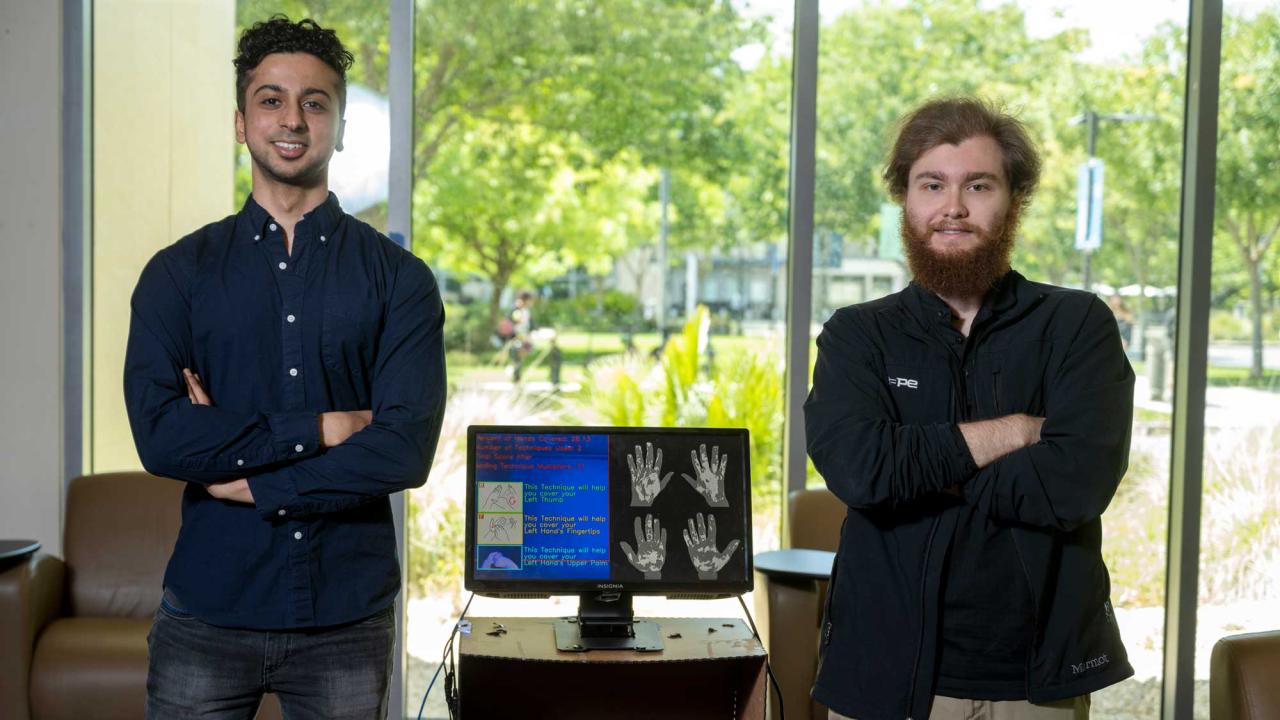 Two men surround a desktop computer with illustration on it