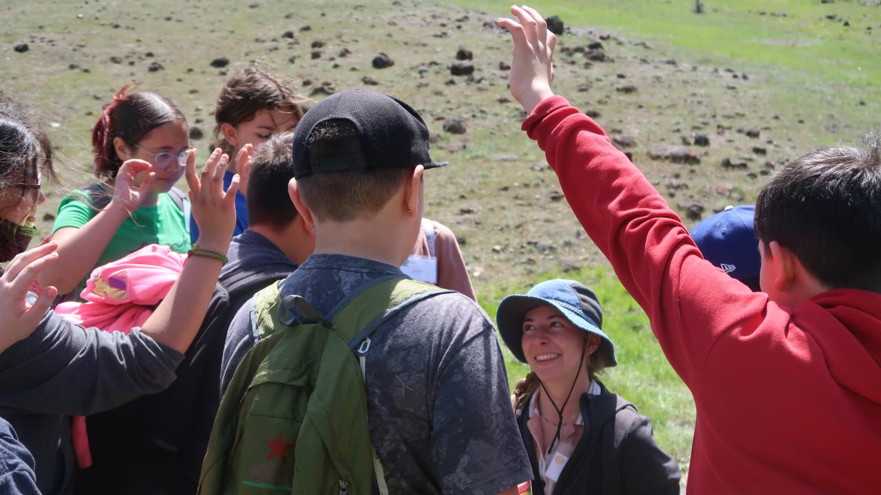 students raise their hands around UC Davis research fellow, Leta Landucci