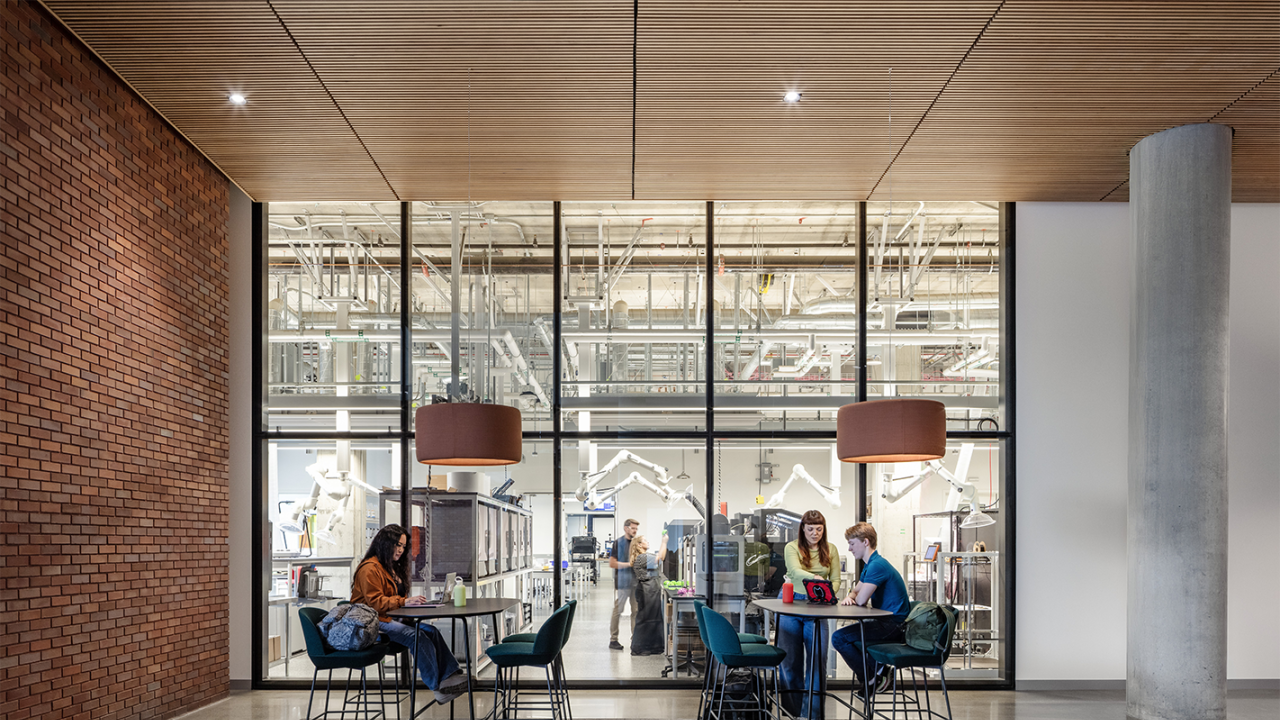 A cozy indoor workspace with dark wood accents and seating, featuring students engaged in conversation against a laboratory backdrop. 