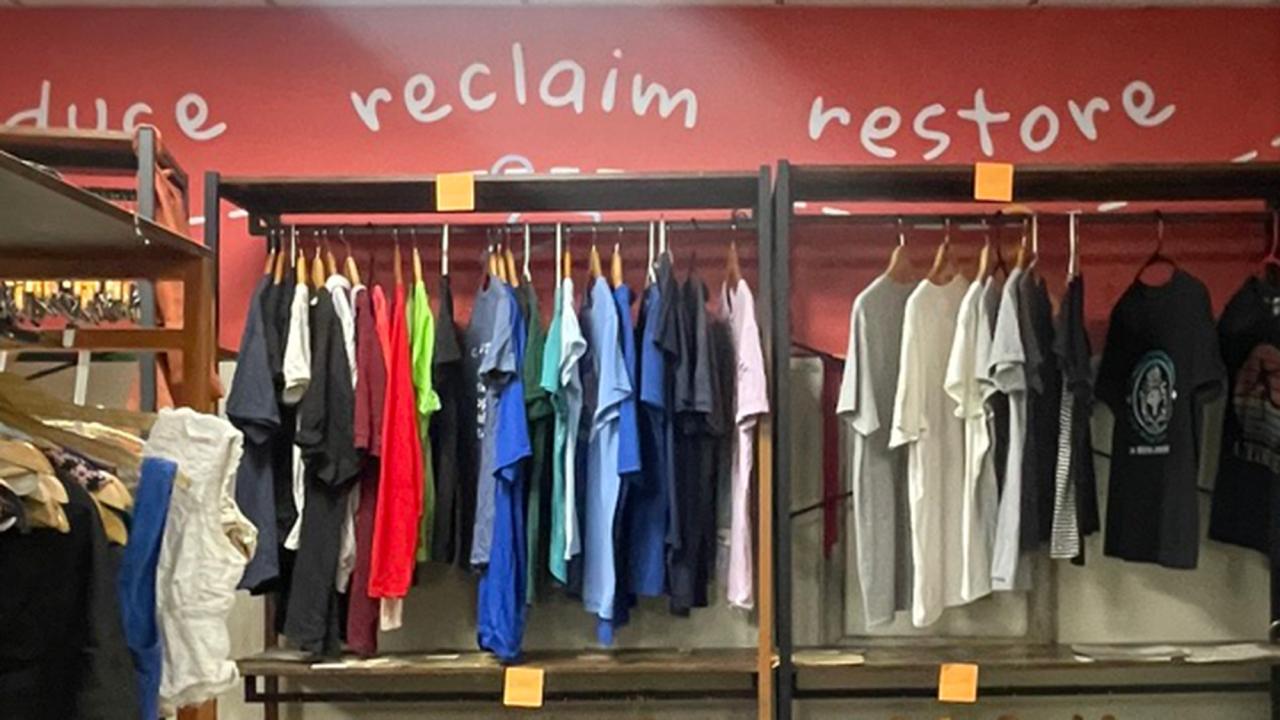 Clothes hanging on a rack, with the words "reclaim" and "restore" painted on the wall behind them.